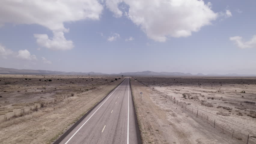 A vast west Texas desert landscape with an empty highway cutting through it, fast moving aerial view