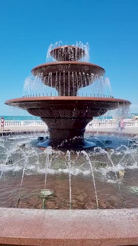 Tiered fountain streams flow in slow motion with bright sunlight and seaside background
