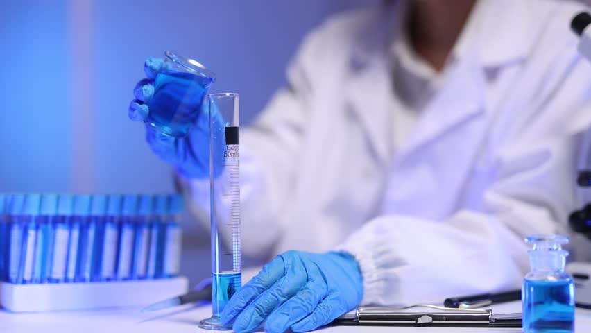 Scientist pouring blue liquid into graduated cylinder in a chemistry experiment.