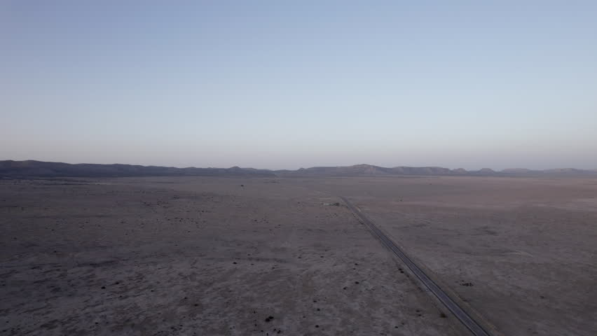 A vast west Texas desert landscape with an empty highway cutting through it, aerial view