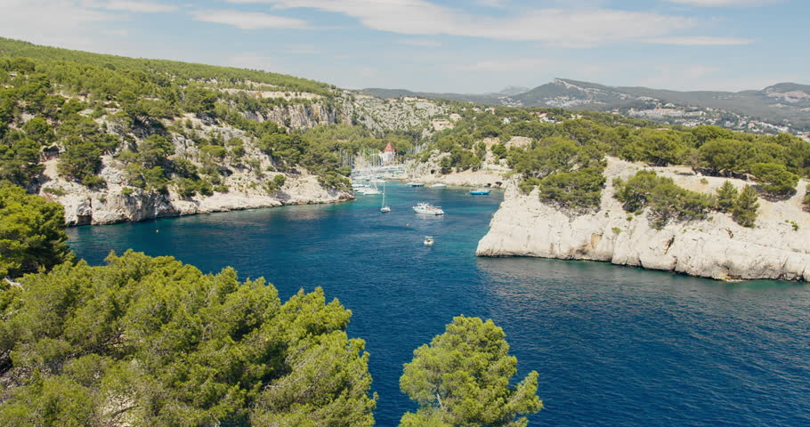 Pleasure boats in Mediterranean calanque with turquoise water and limestone cliffs. Coastal tourism scene in southern France