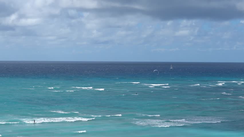 People windsurfing, hydrofoiling, and sailing off the Pacific blue coast of Waikiki, Honolulu, Hawaii on a windy day.