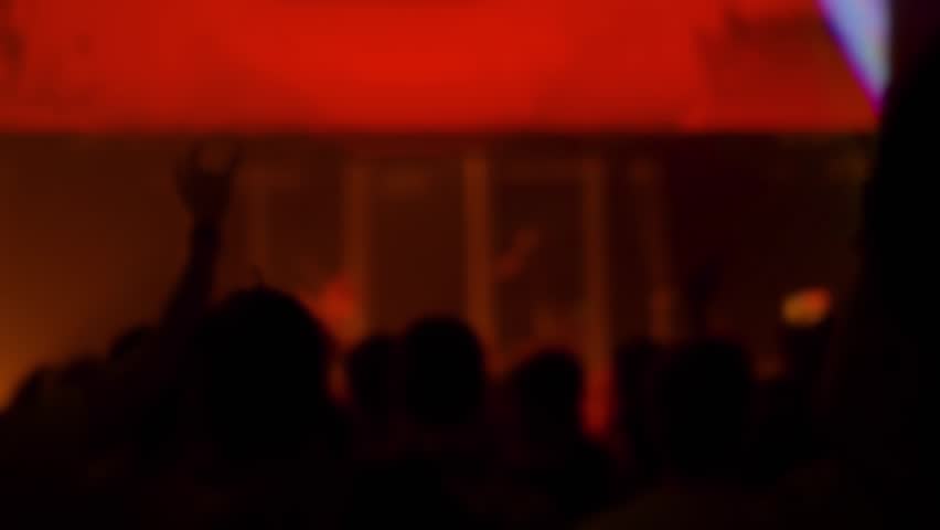 Super slow motion: people crowd partying, cheering, raising hands up and clapping at rock concert in front of stage of nightclub. Bright colorful stage lighting. Nightlife and entertainment concept