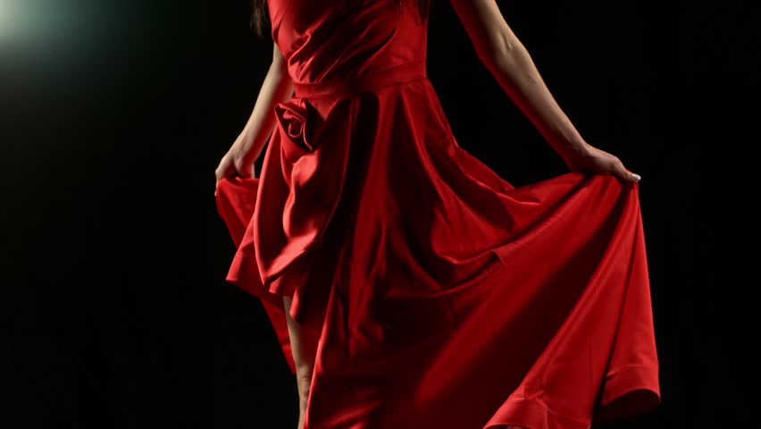 Stunning Black-Haired Woman in Ruby Red Dress and High Heels Gracefully Posing Against a Black Background, Captured in Super Slow Motion. Speed Ramp Effect.