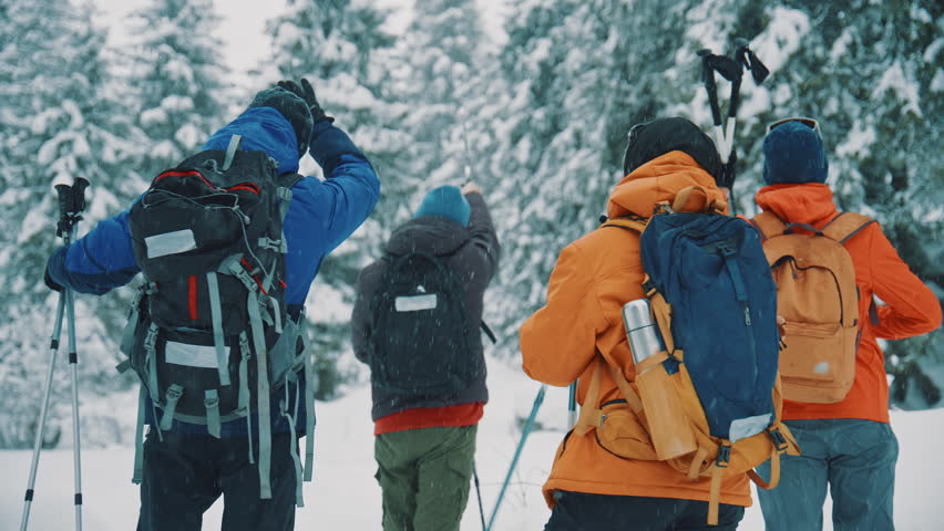 Rear view of a group of friends with backpacks walking through a beautiful snowy forest during a winter blizzard, trekking together on an adventurous journey through the mountain landscape