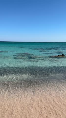 Vertical scenic view of gentle waves washing onto sandy beach with clear turquoise water and calm horizon along Aegean Sea coastline in Greece