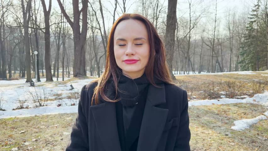 Happy young woman laughing in park, natural female portrait with radiant smile and wearing black coat outdoors.