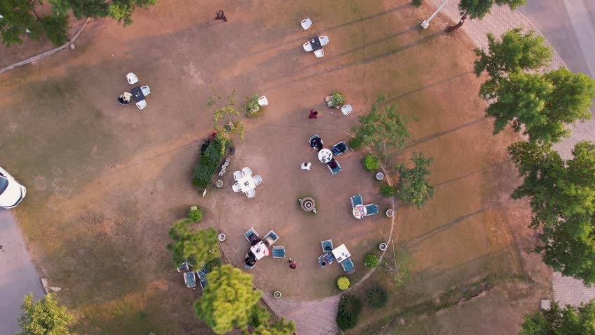 Top-down view of people seated at tables arranged in circular outdoor dining area in park setting