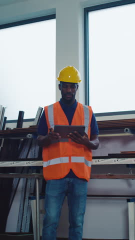 Metal industry worker in a yellow hard hat, monitoring automated system operation, making adjustments via tablet to optimise processes.