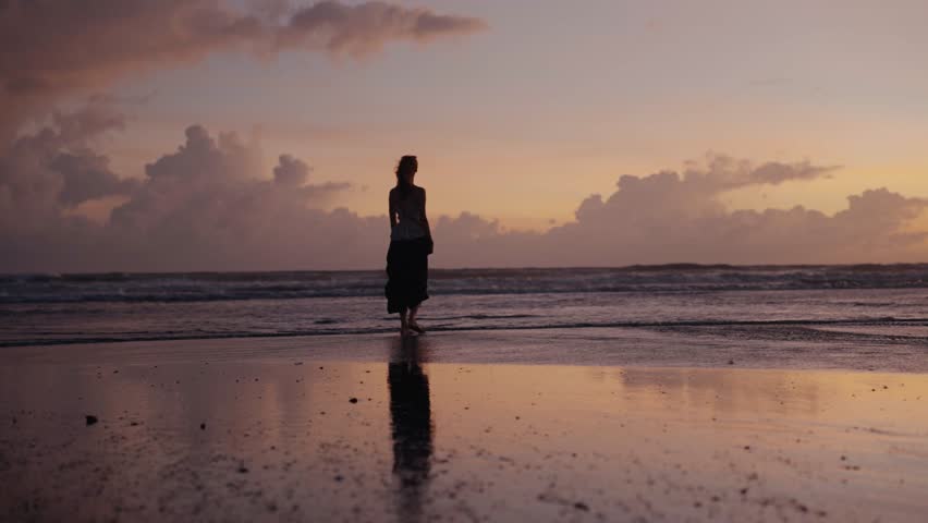 Silhouette of a woman walking on the beach at sunset