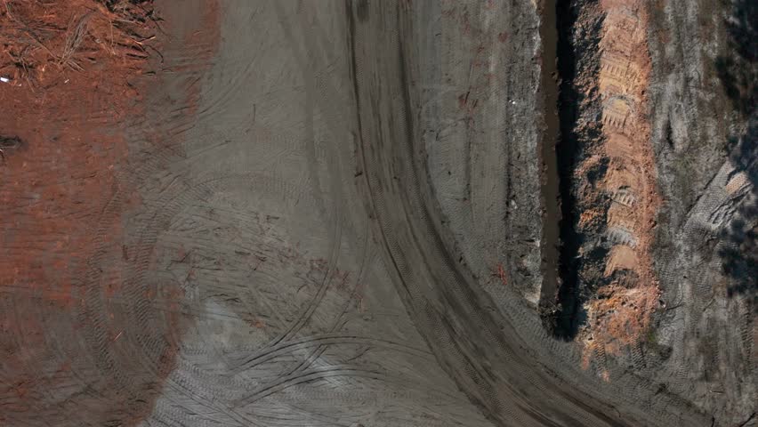 Aerial view of a Caterpillar motor grader on a dirt road on a sunny day. The camera tilted straight down, dolly in over the road following the machine driving.
