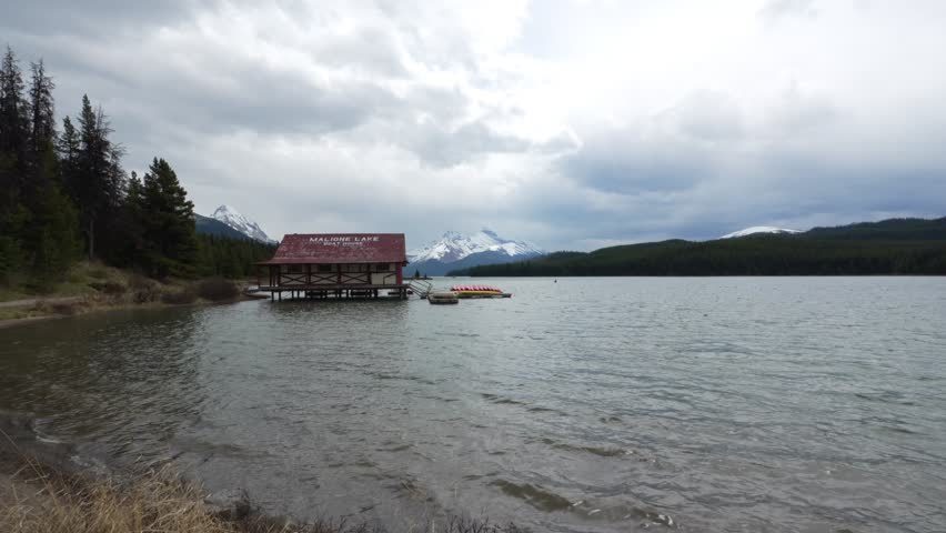 Maligne Lake boathouse on calm water with snow capped mountains and forest in Jasper national park