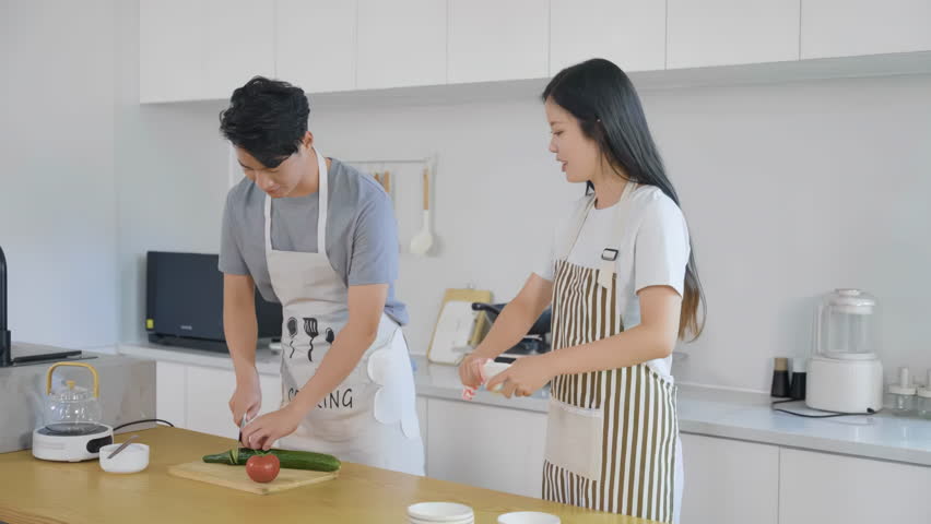 Excited happy young couple in love cooking in the kitchen, playful husband and wife dancing laughing preparing healthy food, romantic family having fun together while making fresh healthy fruits salad