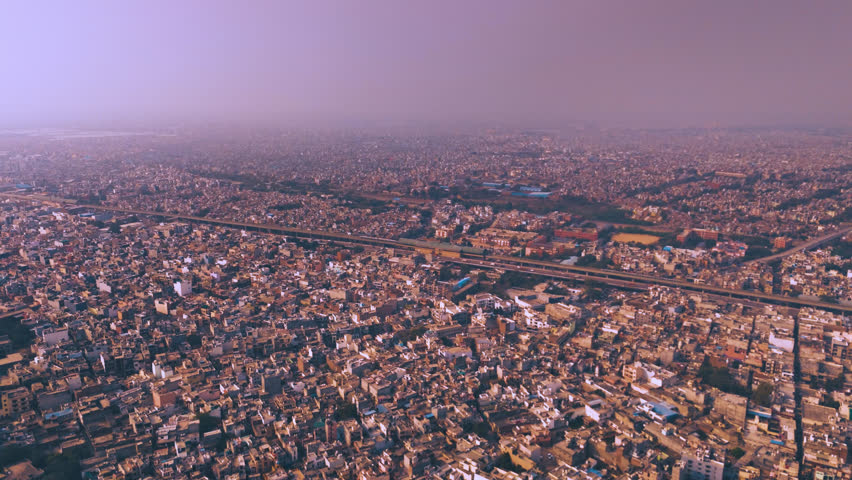 Aerial drone view of dense slum houses in Delhi under warm sunlight with a Delhi Metro Line