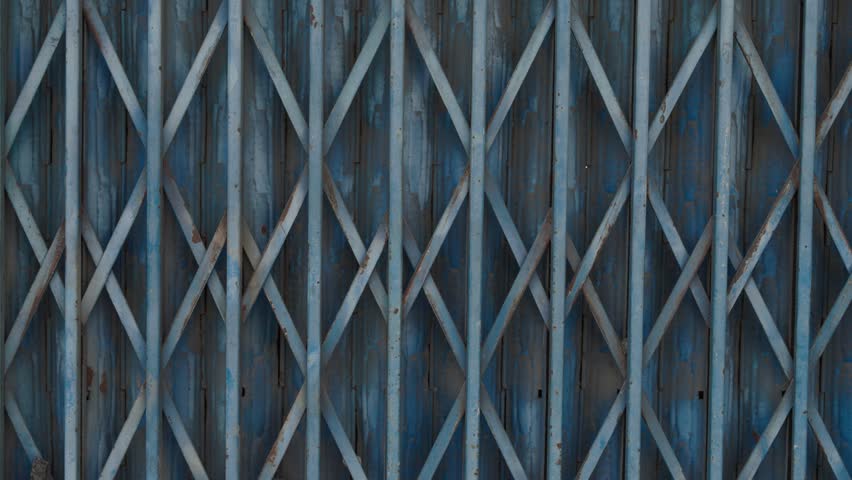 Close-up of blue metal folding gate with geometric pattern. Industrial texture, static shot.