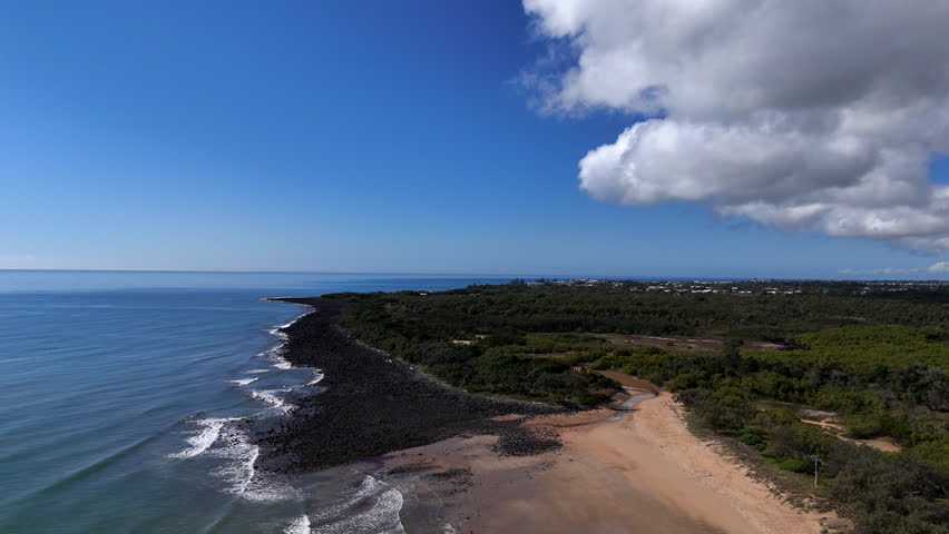 Natural beach landscape with ocean waves and blue sky with scattered clouds.