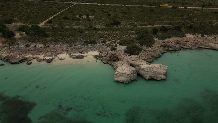 High altitude drone panorama of the Dominican Republic southern coast with a natural rock pool along the shoreline. Turquoise water contrasts with deep blue Caribbean sea in bright tropical daylight.