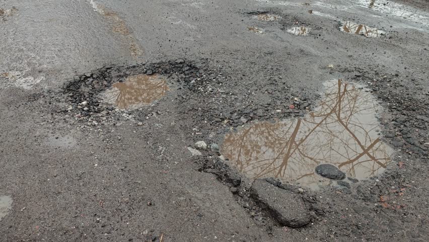 Puddle in broken road with deep pothole after rain 