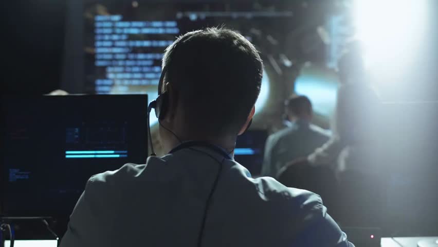 Back view of man in mission control center monitoring satellite flight in orbit, coordinating space mission operations in advanced aerospace environment