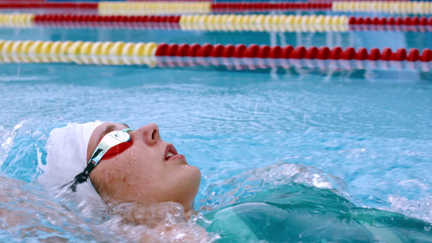 Close-up of a swimmer in a white cap and goggles, performing a freestyle stroke. The swimmer