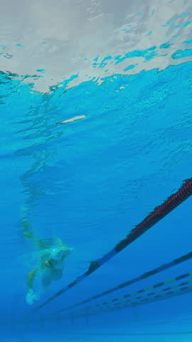 Low-angle shot of a young female swimmer practicing freestyle with black and red swim fins, capturing motion and bubbles.