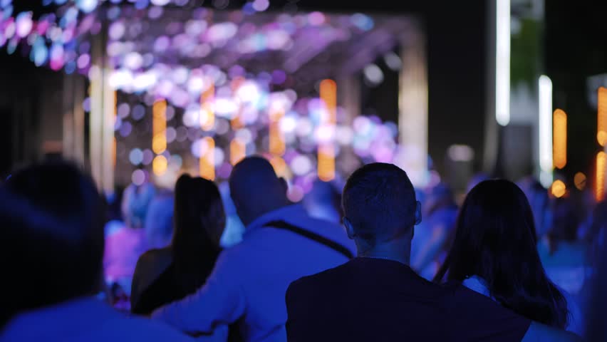 People watching a music festival concert at night with glowing stage lights