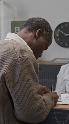 Verical portrait shot of senior African American man turning to look at camera after signing documents at bank counter