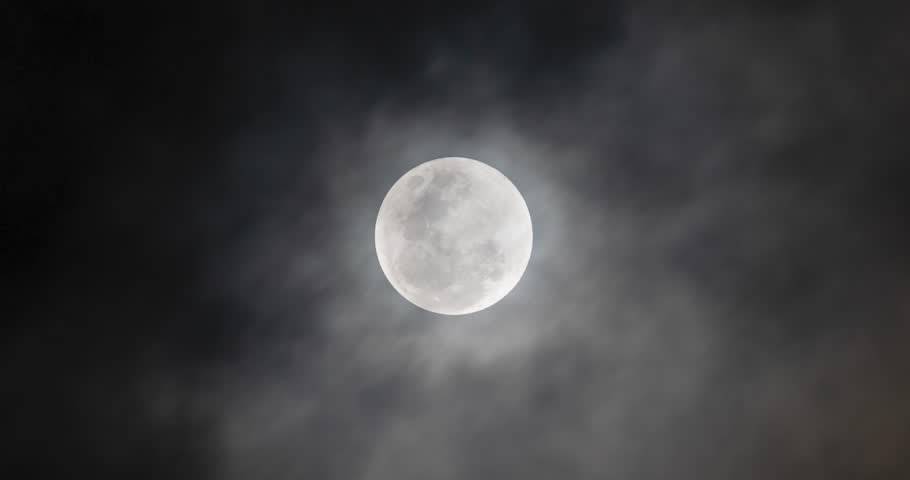 Beautiful zoom in to a shiny full moon through a cloudy night sky