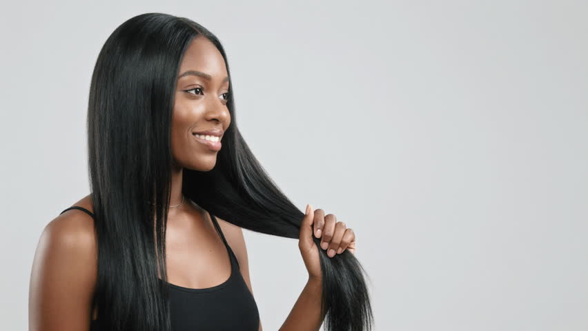 Black woman with sleek straight hair studio beauty influencer demonstrates haircare routine, gently holds and twists long glossy