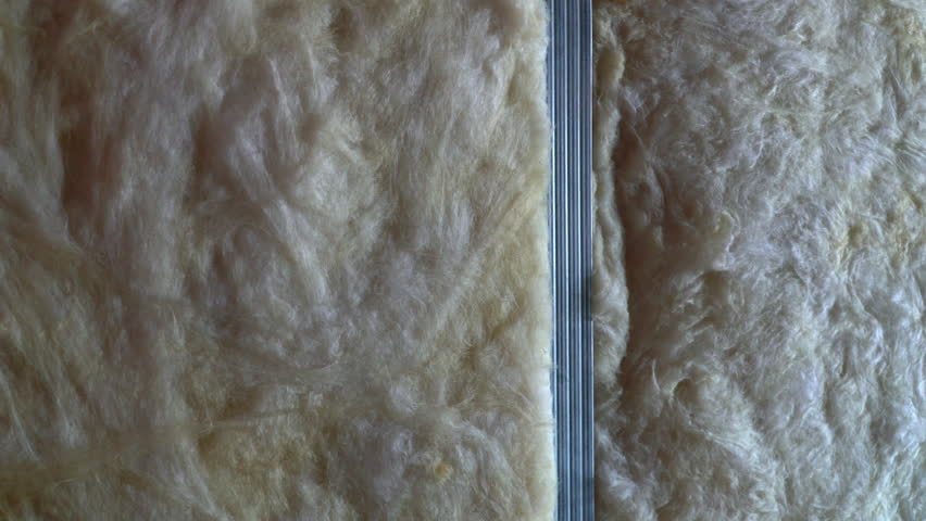 Dense mineral wool insulation material filling the interior of a drywall construction in close-up, soft fibrous texture representing thermal energy efficiency and sustainable building concept.