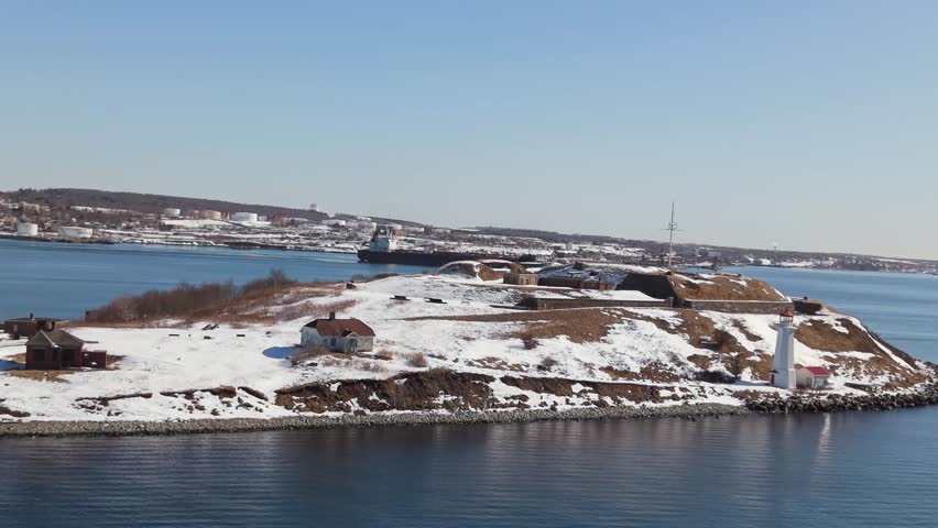 Aerial drone footage: chemical oil tanker sails out of Halifax into open sea. Sunny winter day in Nova Scotia Canada, high speed ship in Halifax Bay, coastal snow visible.