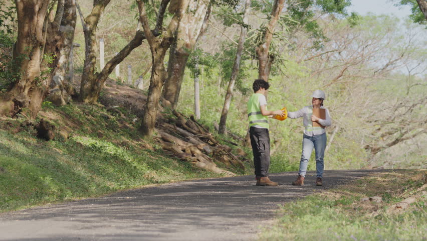 Two engineers, a man and a woman, wearing hard hats and safety vests, discussing a clean energy project on a rural road in a tropical environment near the miravalles volcano in costa rica