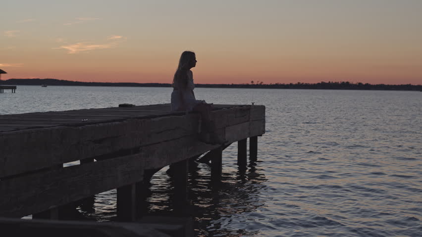 Beautiful Girl sitting on the edge of a dock at sunset with the wind blowing