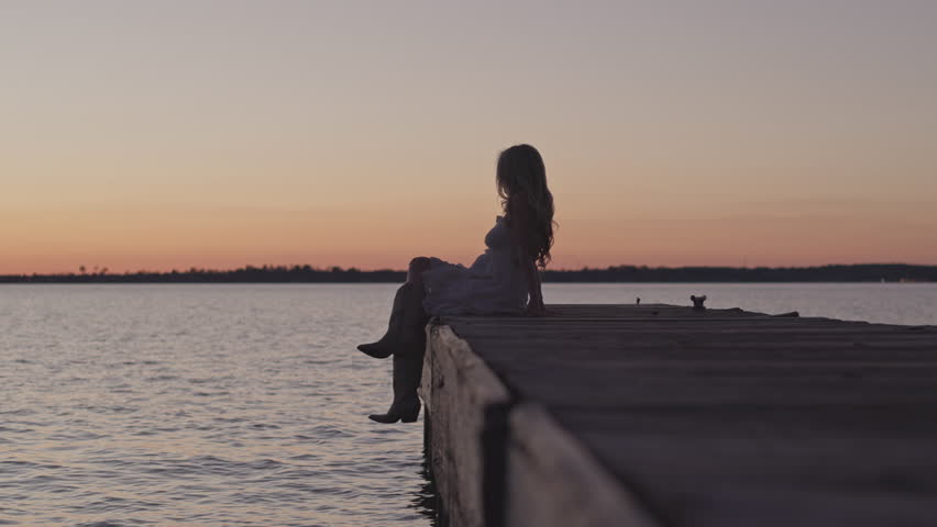 Beautiful girl sitting on a dock at sunset by the lake