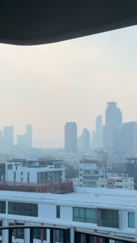 Static wide shot of the Bangkok cityscape obscured by thick smog under a pale sky