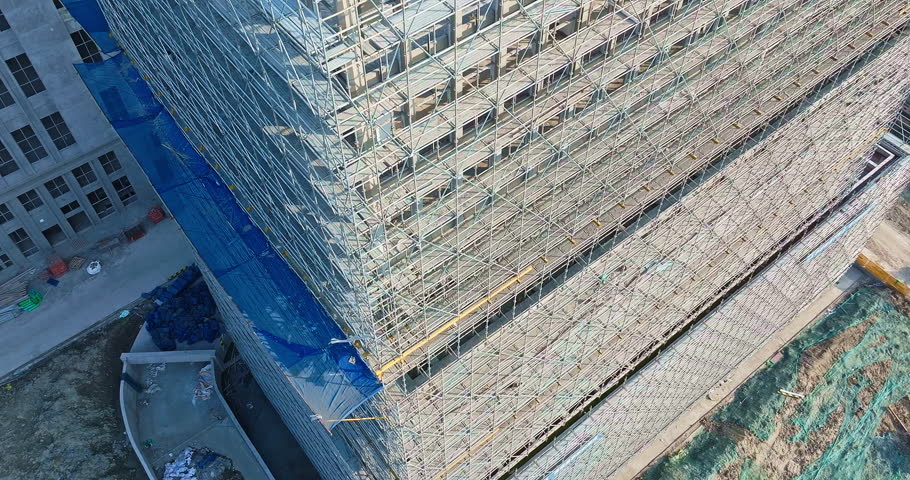 Construction of modern multi-story building featuring extensive metal scaffolding and blue safety nets for urban development.