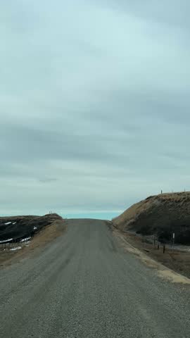 Point of view driving along a backcountry gravel road through open rural landscape with expansive sky and natural surroundings.