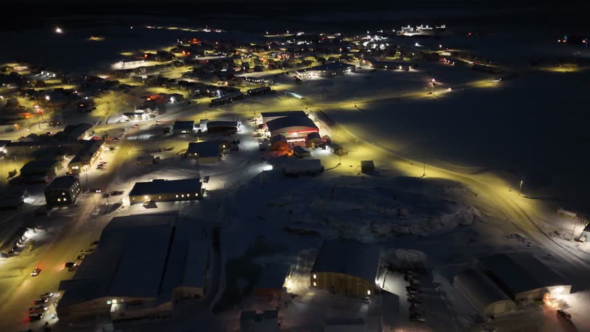 Rankin Inlet, Nunavut Arctic town at night with illuminated houses, streets, and downtown buildings glowing across the snowy northern community along the Hudson Bay coastline under dark skies.
