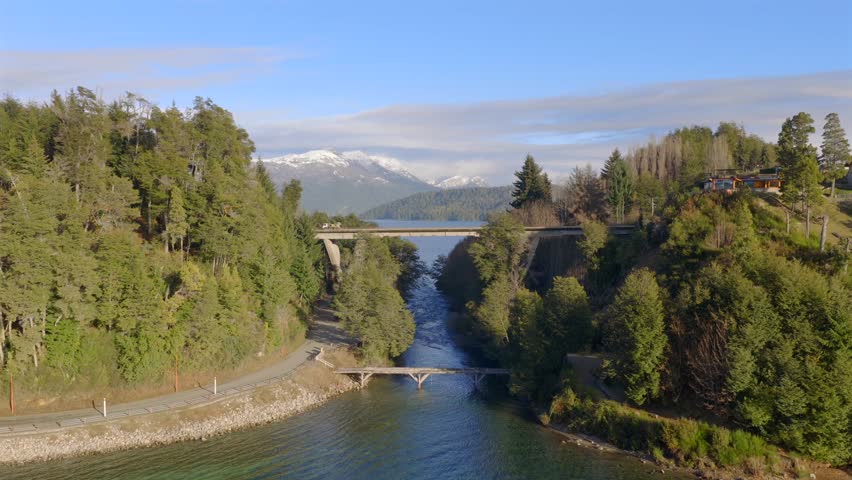 Bridge at Lake Correntoso, Villa la Angostura surrounded by trees, water, and snow-capped mountains. Low aerial approach and under pass in 4K.