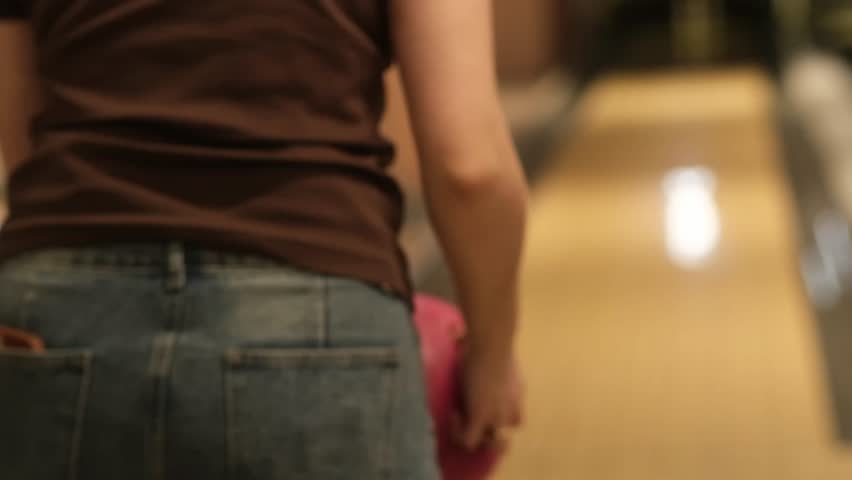 Woman in casual clothing positions herself to bowl, releasing a pink bowling ball down the lane in a lively bowling alley environment