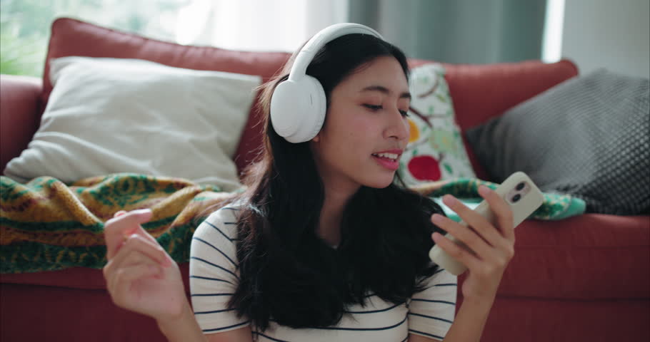 Happy Young Asian Woman Listening to Music with Headphones and Dancing Gently at Home	