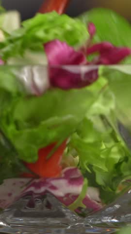 Hand stirs with spoon vegetable salad with mixed lettuce leaves and tomatoes. Cooking food. Vertical shot