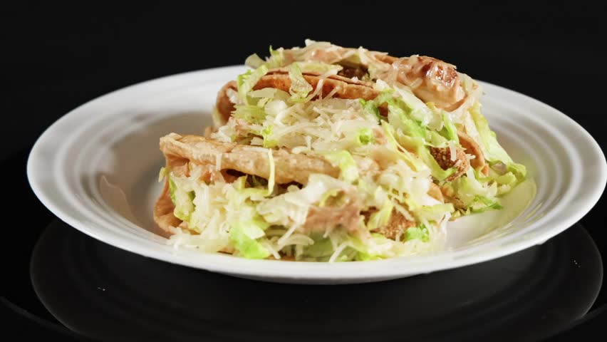 Three hard shell tacos filled with meat and lettuce rotate slowly on a white plate.