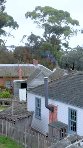 A vertical shot of a traditional wooden cottage with smoke drifting from its chimney.