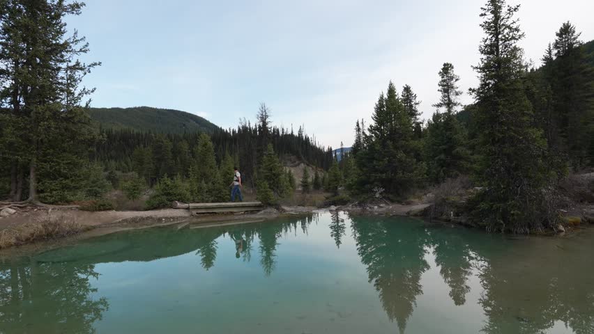 Hiker walking past the mineral rich pools of the Ink Pots surrounded by forest and mountains in Banff National Park