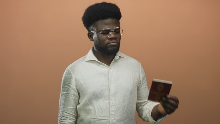Man holding red passport and finger pointing to passport in studio against peach wall; travel confidence.
