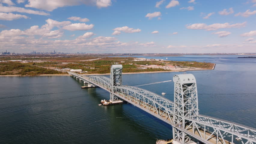 Aerial drone view of the Marine Parkway Bridge connecting Brooklyn and Queens over calm water with sandy shoreline and coastal landscape, filmed in ProRes 422HQ.