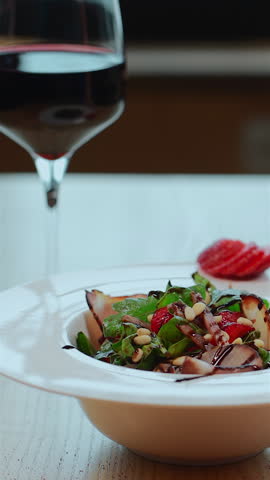 closeup of salad with arugula, meat ham and strawberry or glass of wine on table