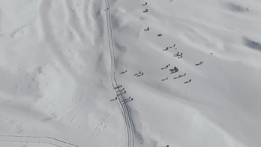 Wide aerial shot of hikers snowshoeing across snowy mountain terrain. Outdoor winter expedition and adventure travel concept in pristine landscape.