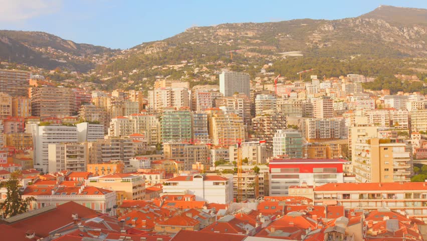 Wide panoramic view of Monaco city skyline with residential buildings and mountains in the background on a sunny day.